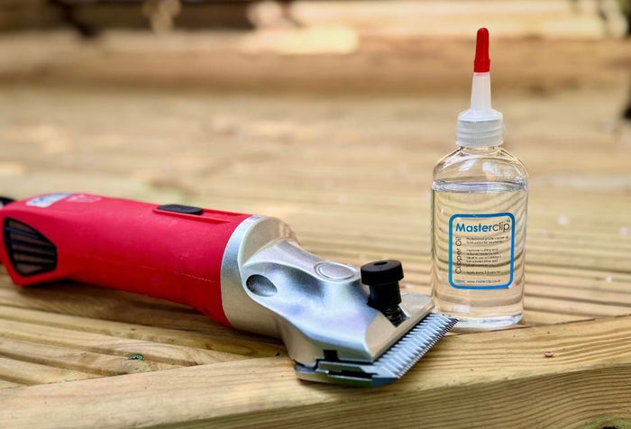 A red horse clipper on placed next to a bottle of clipper oil on a wooden platform